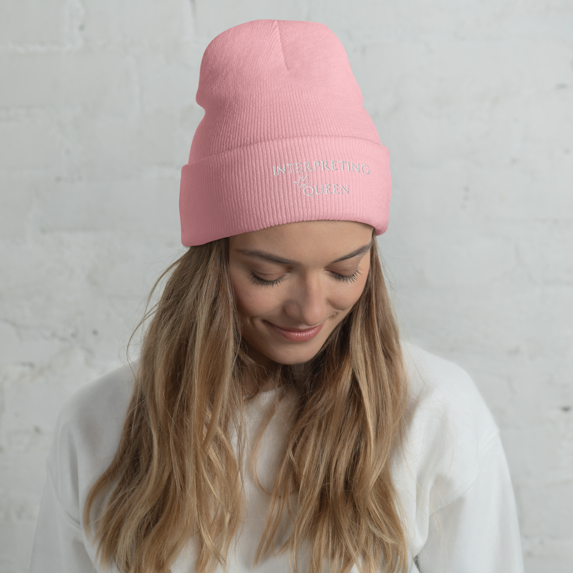Pink beanie hat with white text "Interpreting Queen" with a small crown on top of the letter Q in Queen.