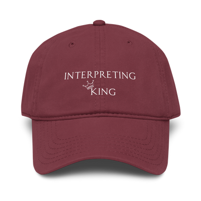 Red baseball cap with white text "Interpreting King" with a small crown on top of the letter K in King.