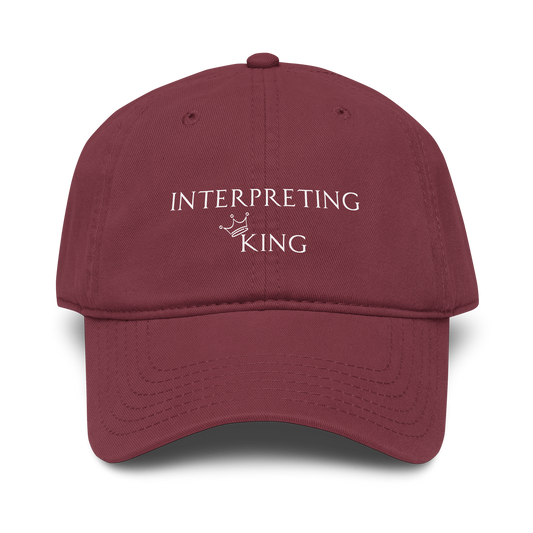 Red baseball cap with white text "Interpreting King" with a small crown on top of the letter K in King.